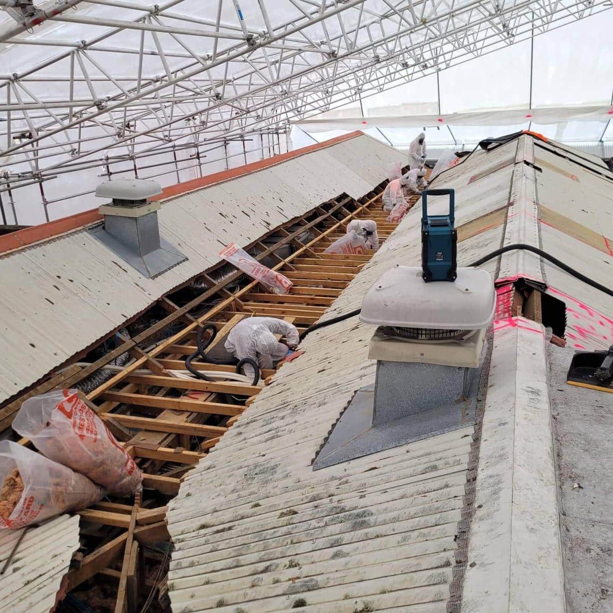 Workers in protective clothing remove asbestos from a roof.