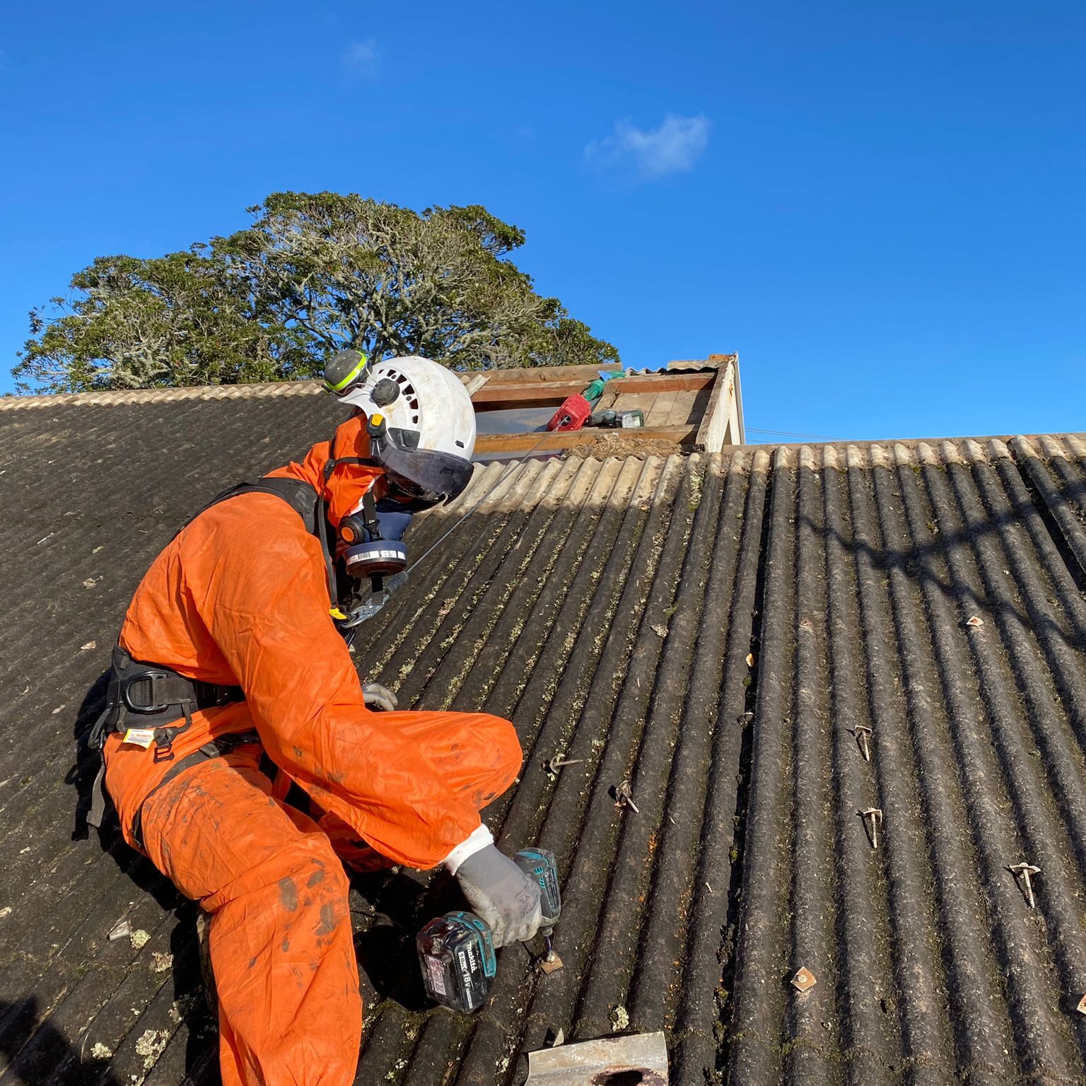 An asbestos removal expert in full safety gear working on a roof removing asbestos