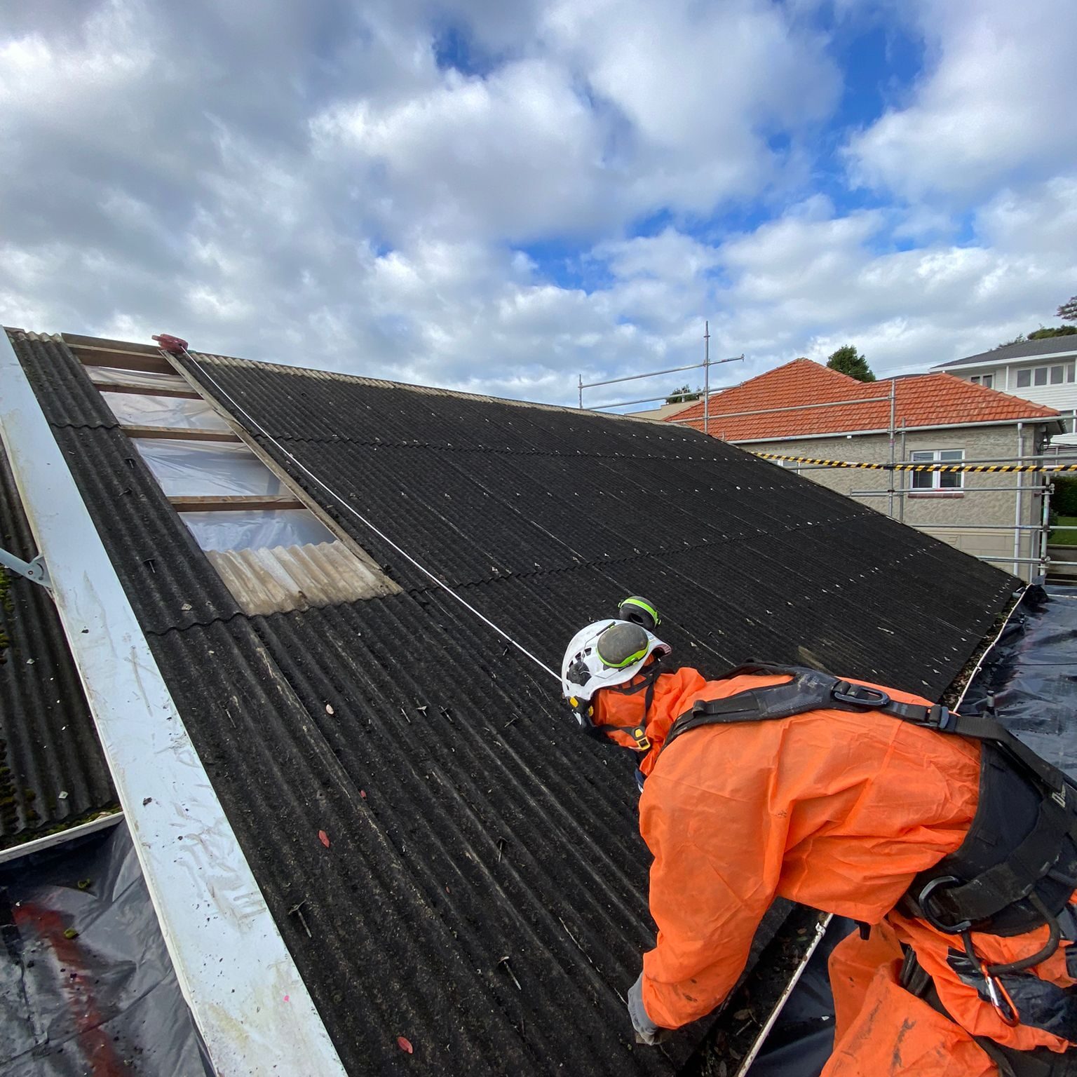 A asbestos removal worker in safety gear working on a Class B Asbestos roof removal