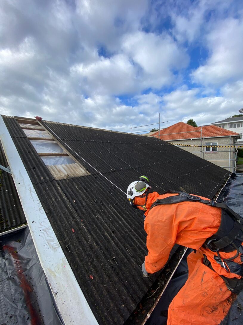 A asbestos removal worker in safety gear working on a Class B Asbestos roof removal